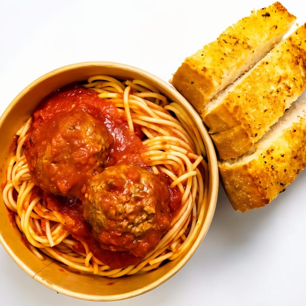Spaghetti with meatballs and red sauce in a bowl, with two slices of garlic bread.